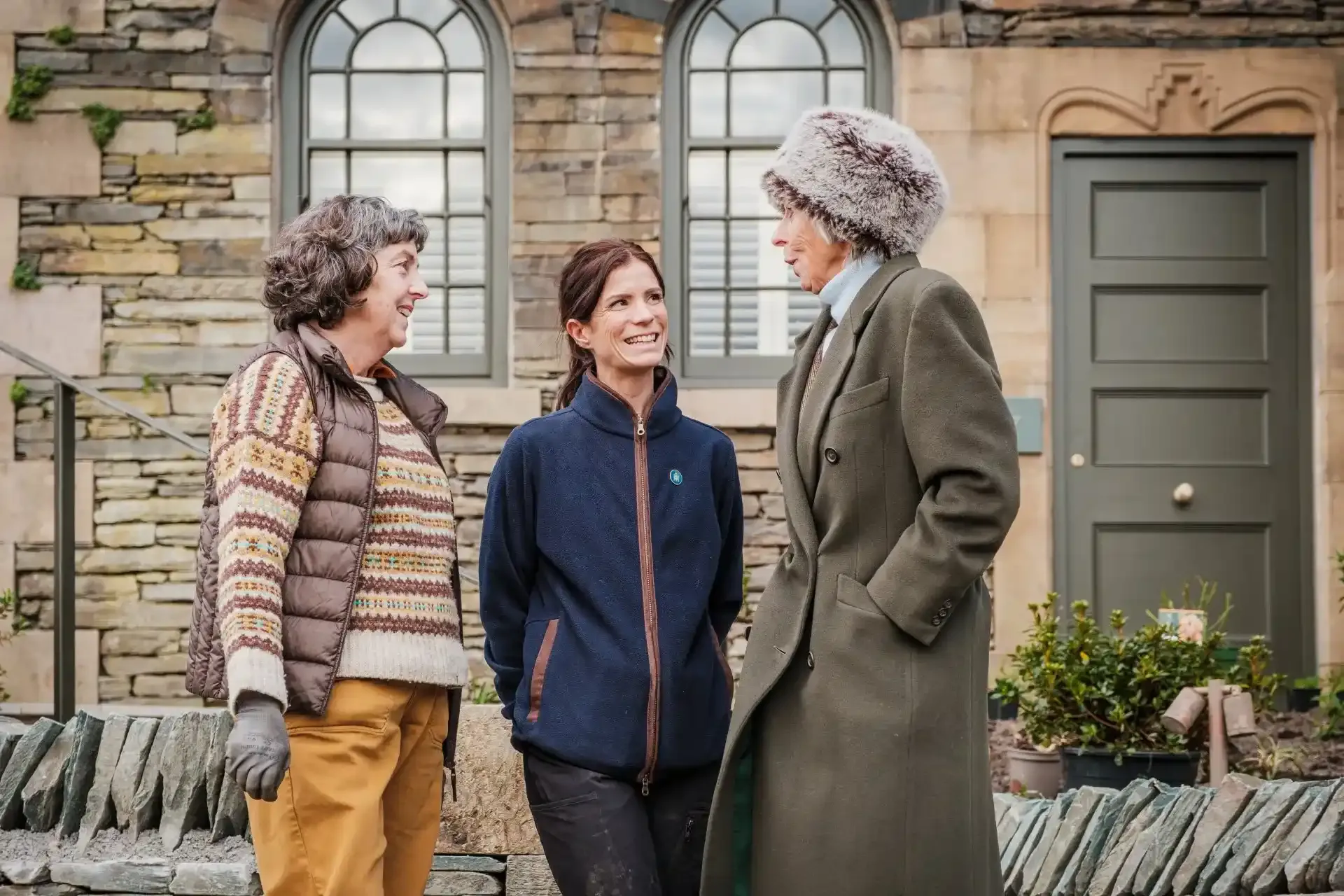 Three women talking and smiling in front of a building.