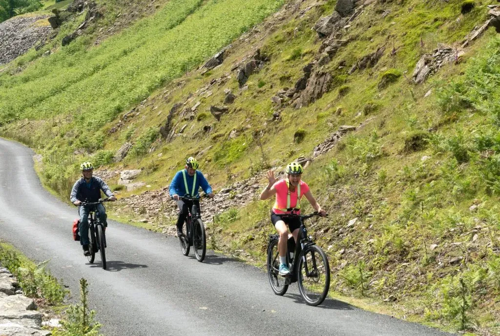 people biking on a road surrounded by green hills