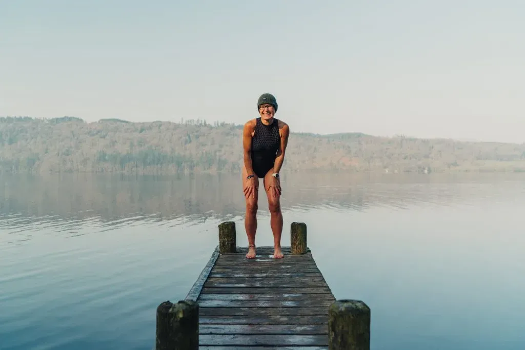 woman posing in bathing suit and cap on a dock overlooking the lake and forest