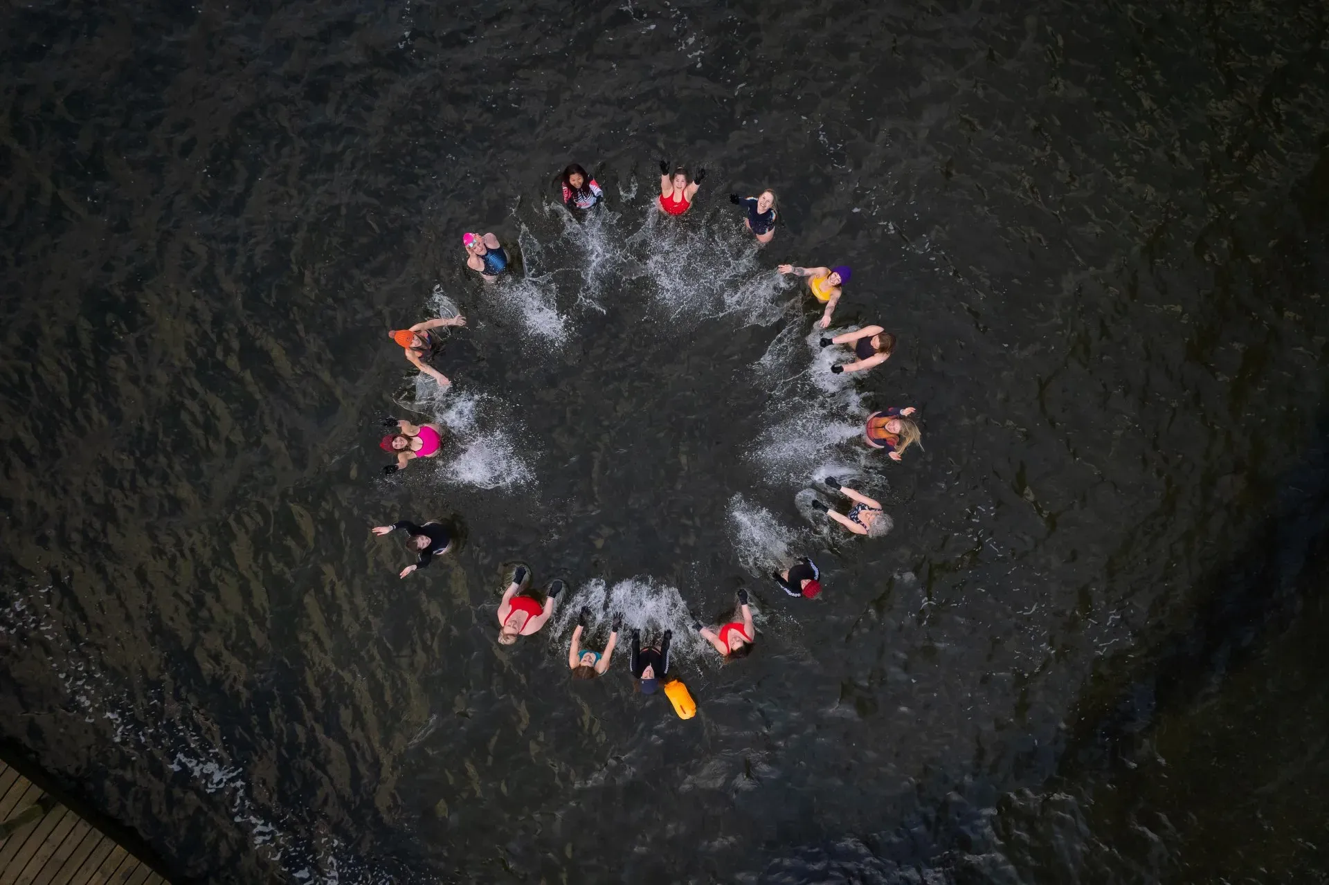 group of swimmers forming a circle in a lake while wearing colourful bathing suits